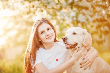 Güzel kız yaz parkında Labrador Retriever köpeğine sarılıyor, gün batımında. Hayvanlar en iyi arkadaş konsepti