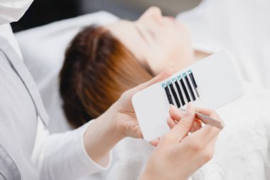 Usta sahte kirpik uzatma prosedürünü kadın için cımbızla yapıyor.