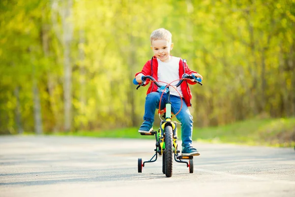 Rapaz feliz anda de bicicleta e sorri no parque de verão. Conceito de treinamento de passeio — Fotografia de Stock