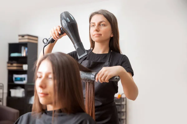 Drying long shine brown hair with dryer and round brush. Beauty shop — Stock Photo, Image