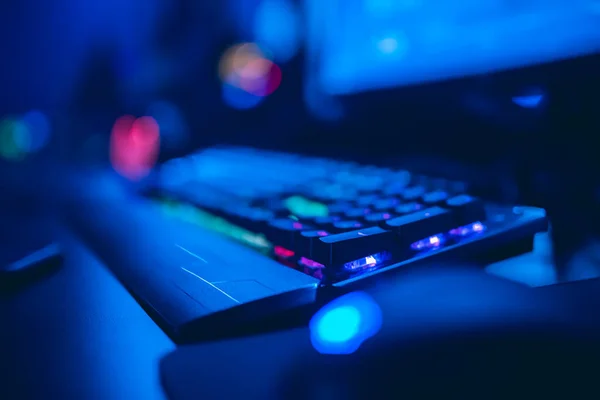 Jugador profesional jugando torneos de juegos en línea ordenador PC con auriculares, fondo rojo y azul borrosa —  Fotos de Stock