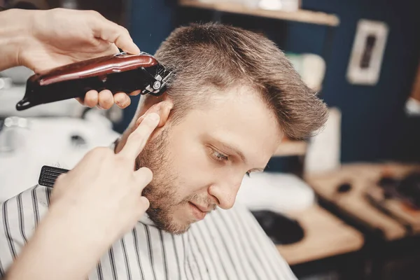 Kapper in kapperszaak scheren haar elektrisch naar jonge man voor modieuze kapsel — Stockfoto