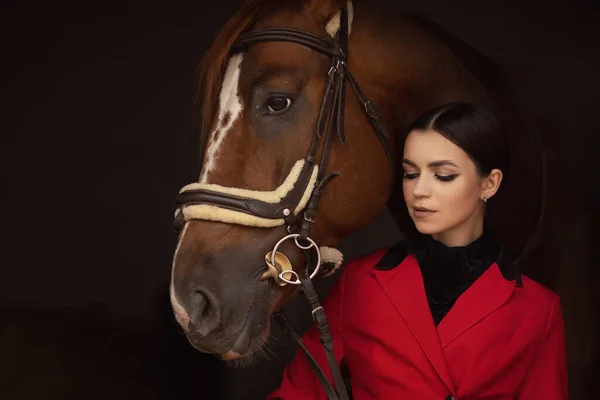 Rider jockey γυναίκα αγκαλιάζει με καφέ άλογο, μαύρο φόντο — Φωτογραφία Αρχείου