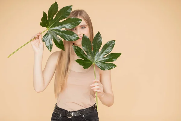 Bella ragazza bionda con la pelle pulita tiene foglia verde su sfondo beige. Beauty spa cura crema concetto — Foto Stock