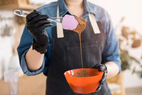 Pasticcere giovane donna in grembiule prepara caramelle dolci, scioglie il cioccolato in ciotola — Foto Stock