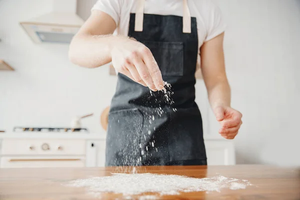 Chef in grembiule spruzza farina con mano su pasta, tavolo in legno, fondo chiaro — Foto Stock