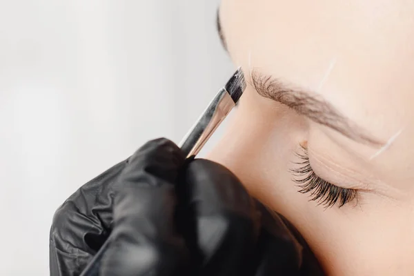 Correctie en tint van wenkbrauwen, meester brengt borstel aan op vrouw markering op de wenkbrauw — Stockfoto