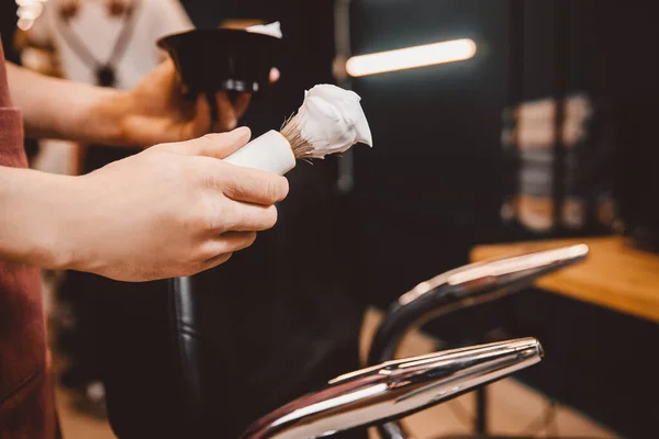 Közelkép borotva kezében borbély, háttér ügyfél vár borotválkozás szakáll és bajusz — Stock Fotó