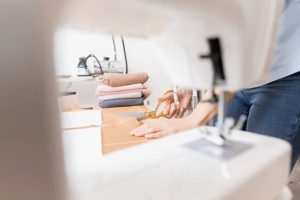 Lugar de trabajo del sastre costurera. La diseñadora joven corta el patrón de la tela de la línea del boceto con las tijeras para adaptar los vestidos y la ropa — Foto de Stock