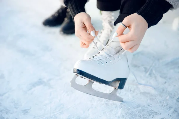 Menina amarra cadarços em patins figura branca para pista de gelo no inverno. Natal feriados conceito — Fotografia de Stock