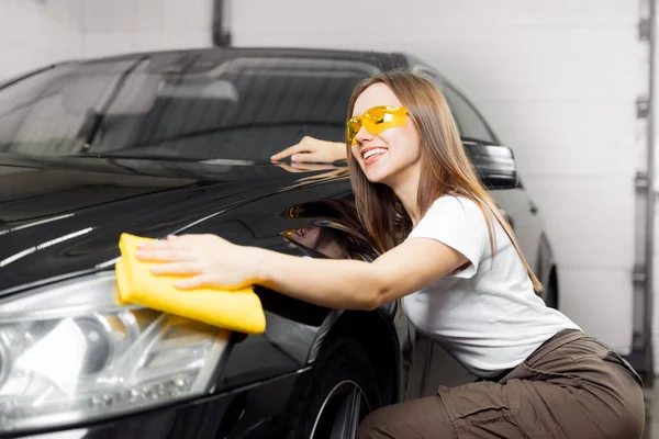 Servicio de lavado de coches, trabajador hermosa chica pulidos y limpios faros de microfibra en auto negro —  Fotos de Stock