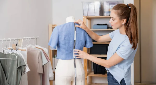 Jovem seamstress trabalhando com fita métrica para tirar medidas do manequim — Fotografia de Stock