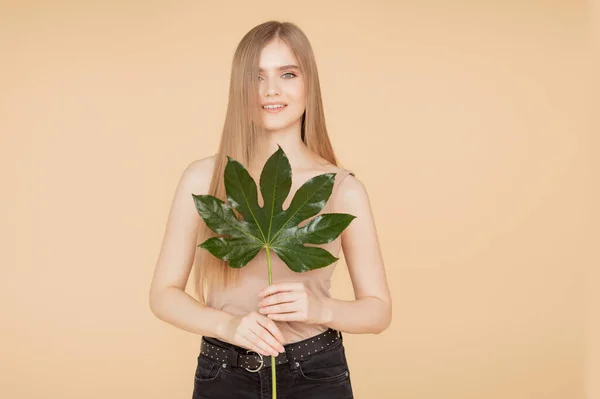 Hermosa chica rubia con la piel limpia sostiene hoja verde sobre fondo beige. concepto de crema de cuidado spa belleza —  Fotos de Stock