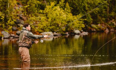 Fisherman using rod fly fishing in river morning standing in water clipart