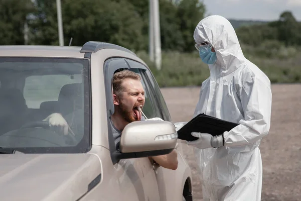 Γιατρός με προστατευτική στολή ιού που παίρνει μάκτρο από τον οδηγό προσώπου για να εξετάσει για λοίμωξη από τον ιό του στομίου COVID-19 — Φωτογραφία Αρχείου