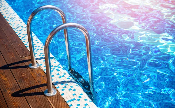 Blue swimming pool with grab ladder teak wood flooring stripes sunlight — Stock Photo, Image