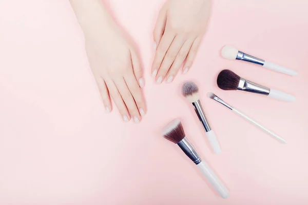 Weibliche Hand mit Make-up-Pinseln auf rosa Hintergrund. Aussichtspunkt von oben, flache Lage — Stockfoto