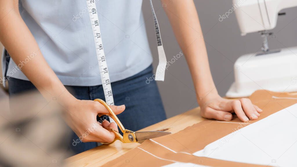 Young female designer cuts out pattern of fabric from sketch line with scissors for tailoring dresses and clothes