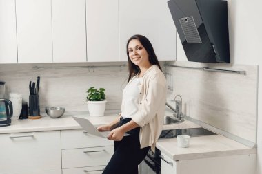 Genç kadın mutfaktaki dizüstü bilgisayarın arkasında çalışıyor. izolasyon işçisi konsepti