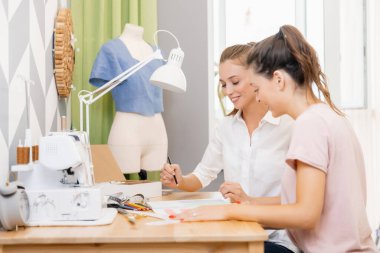Öğretmen kadın öğrencilere yardım ediyor. Elbise dikiyor, moda ve tasarım okuyor.
