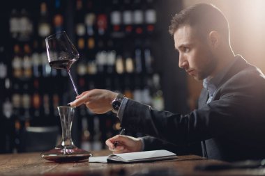 Sommeliers erkeği kırmızı şarabı tadıyor ve aroma degukasyonu kartı yazıyor.