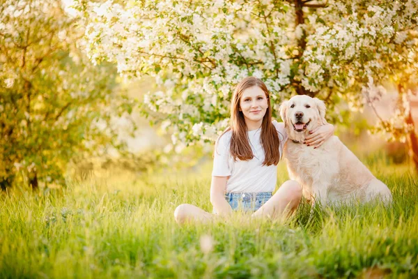 Young woman hugs dog Labrador Retriever outdoors in park, sunny day. Animals best friends concept