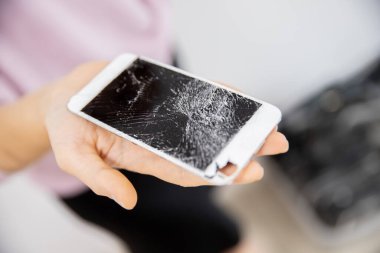 Kadının ellerinde kırık cam bir telefon ekranı, beyaz arka plan.