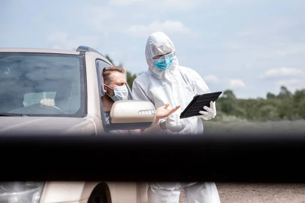 Concepto prohibición conductor coche viaje coronavirus. Médico en traje protector y máscara en zona de control covid-19 muestra gesto de stop — Foto de Stock