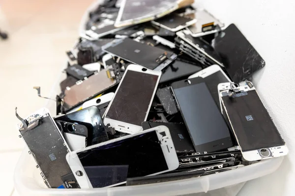 РОССИЯ - 27 июля 2020 года: сломанные экраны iPhone, крупный план подержанных аккумуляторов мобильных телефонов, планшетных панелей, ноутбука, собранного для утилизации в пластиковой упаковке inmrepair и greenpeace — стоковое фото