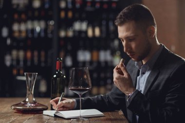 Sommeliers erkeği kırmızı şarabı tadıyor ve aroma degukasyonu kartı yazıyor.