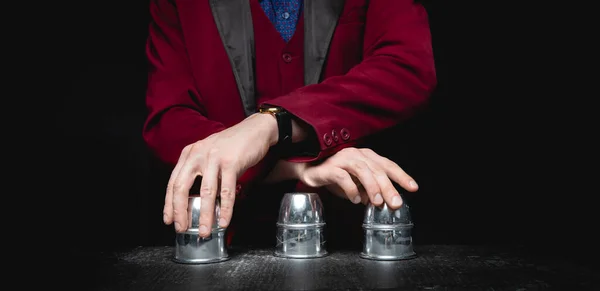 Magician shows shell game of thimbles with circles and ball, black background. Concept deception, sleight hand — Stock Photo, Image