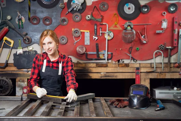 Hermosa mujer sonrisa carpintero y soldador en el lugar de trabajo de fábrica. Fabricación de estructuras metálicas, medidas tamaño de la regla — Foto de Stock