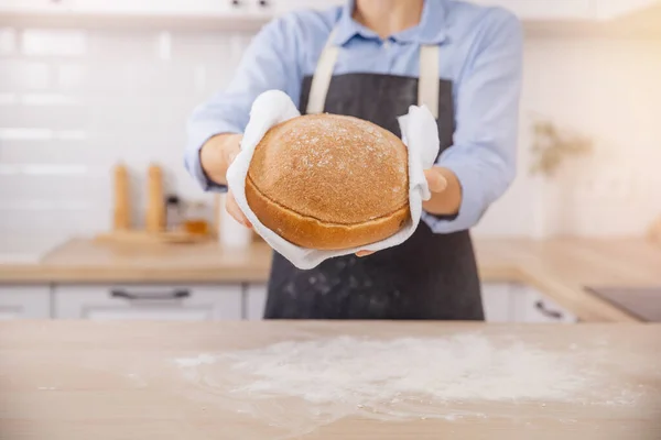 Kéz pék kezében kerek kenyér fehér. Nő kötényben otthon Skandi konyha háttér — Stock Fotó