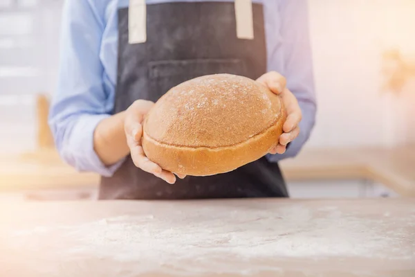 Baker kézzel búzázott kerek kenyér fekszik az asztalon liszt, fehér konyha háttér — Stock Fotó