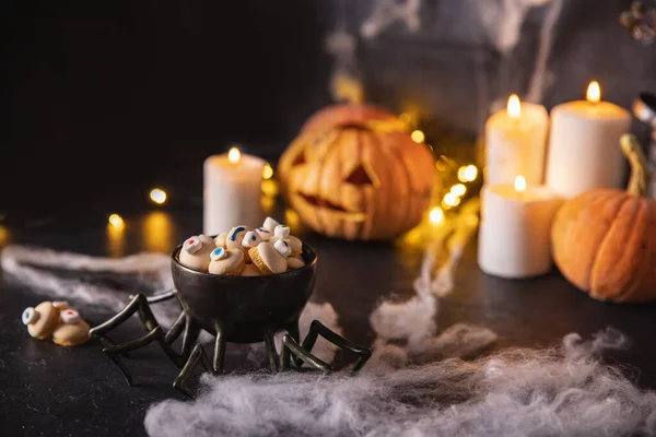Caramelos y galletas en forma de ojo para las vacaciones de halloween, fondo oscuro con telarañas, calabazas y velas — Foto de Stock