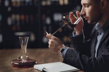 Sommelier restoran için alkol tatma kartı hazırlıyor, bardaktaki kırmızı şarabı değerlendiriyor.