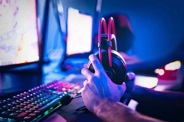 Jugador cibernético profesional jugando torneos en línea ordenador con auriculares, fondo rojo y azul borroso —  Fotos de Stock