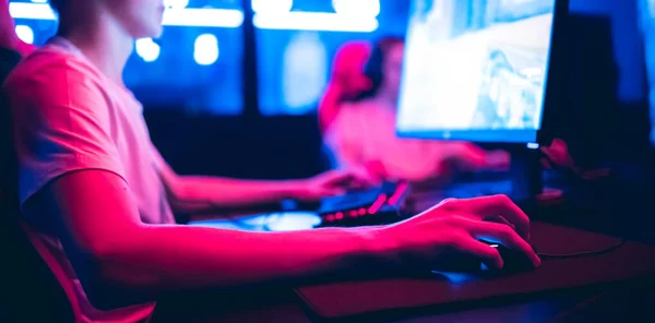 Jugador profesional jugando torneos de juegos en línea ordenador PC con auriculares, fondo rojo y azul borrosa — Foto de Stock