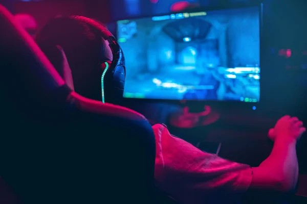 Jugador profesional jugando torneos de juegos en línea ordenador PC con auriculares, fondo rojo y azul borrosa —  Fotos de Stock