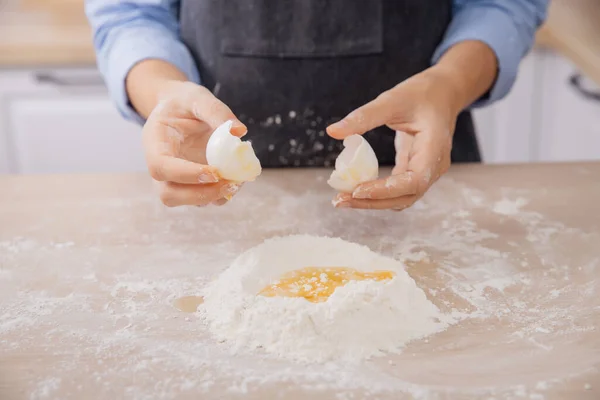 A nő szakács feltöri a tojást lisztté, gyúrja a tésztát a fehér konyhában. Mozgásban a fotográfia — Stock Fotó