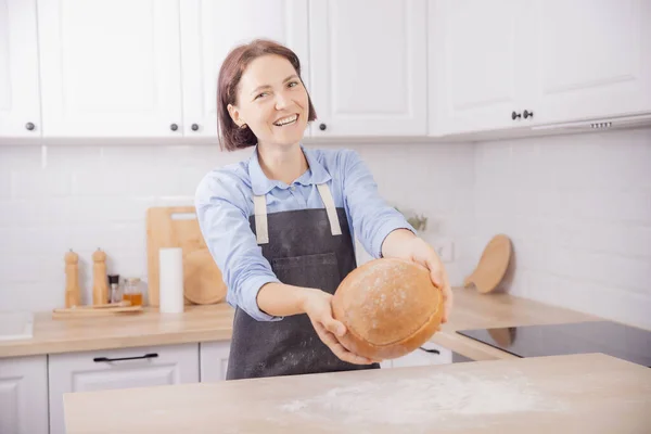 Kéz pék kezében kerek kenyér fehér. Nő kötényben otthon Skandi konyha háttér — Stock Fotó