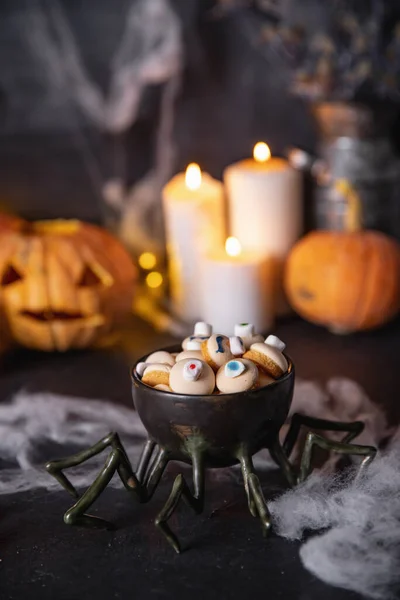 Caramelos y galletas en forma de ojo para las vacaciones de halloween, fondo oscuro con telarañas, calabazas y velas — Foto de Stock