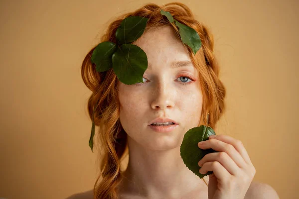 Hermosa joven pelirroja con pestañas extendidas y ojos azules, sostiene hojas verdes naturales en la boca. Bio útil cosmetología concepto de moda —  Fotos de Stock