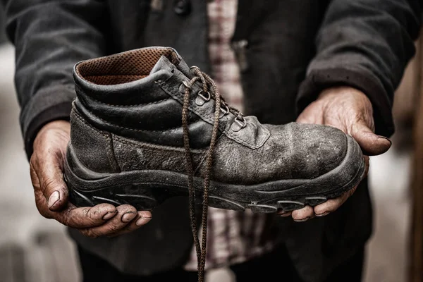 Um sem-abrigo segura uma bota velha e suja com as mãos. Reparação de sapatos, conceito de pobreza — Fotografia de Stock