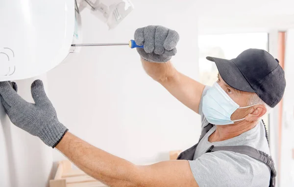 Técnico homem em máscara médica trabalhador de reparação e instala ar condicionado na parede branca — Fotografia de Stock