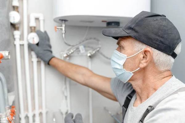 Encanador masculino em máscara médica verifica tubos para abastecimento central de água quente e fria do apartamento — Fotografia de Stock