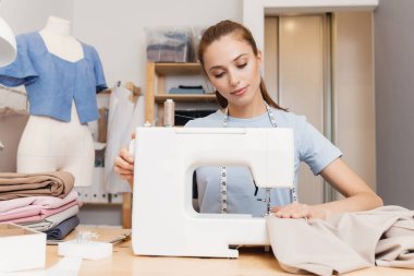 Dikiş dikme işlemi, terzi kız stüdyoda dikiş makinesinde çalışıyor, arka planda manken.