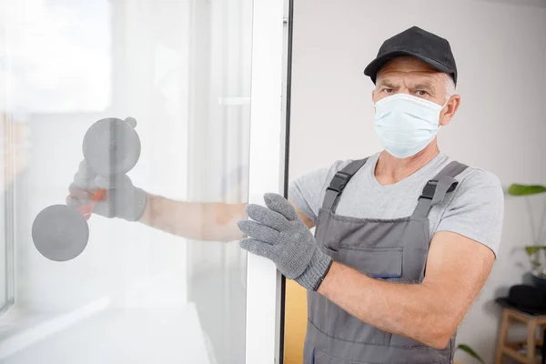 Munkás férfi orvosi maszk telepíti műanyag upvc ablakok és ajtók fehér vákuumemelő — Stock Fotó
