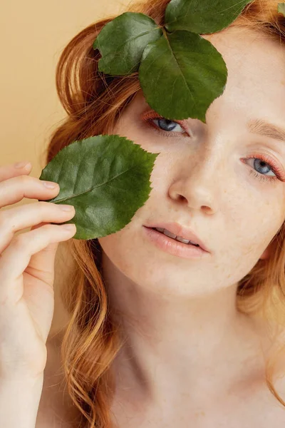 Hermosa joven pelirroja ojos azules con hojas verdes en la cara. Naturaleza cosmética orgánica y maquillaje —  Fotos de Stock