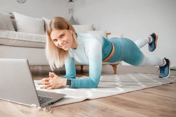 Entrenamiento de fitness en línea en casa, mujer viendo videos trabajando en computadora portátil, entrenando yoga mientras navega por la web —  Fotos de Stock